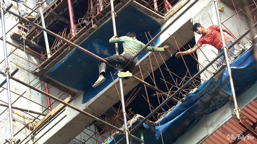 Without any safety gear, two labourers work at an under-construction high rise