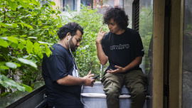 Two friends in one frame, one is talking and the other is listening to music